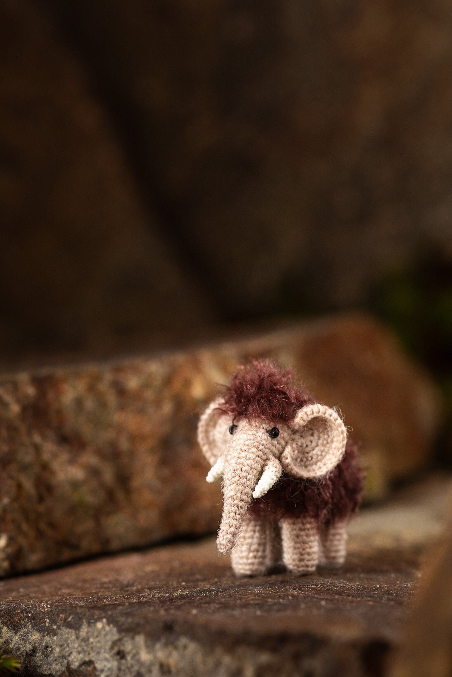 Tiny crochet woolly mammoth on stone background