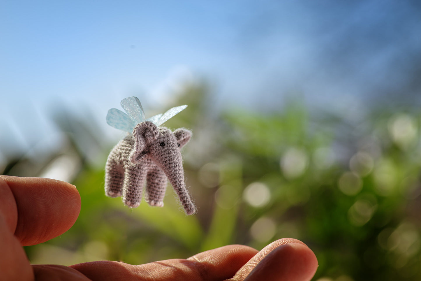 Tiny crochet elephant with translucent wings floating in sunlight