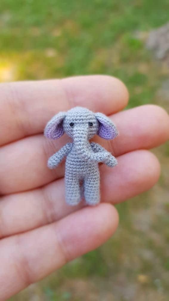Tiny crochet elephant standing on a human fingertip