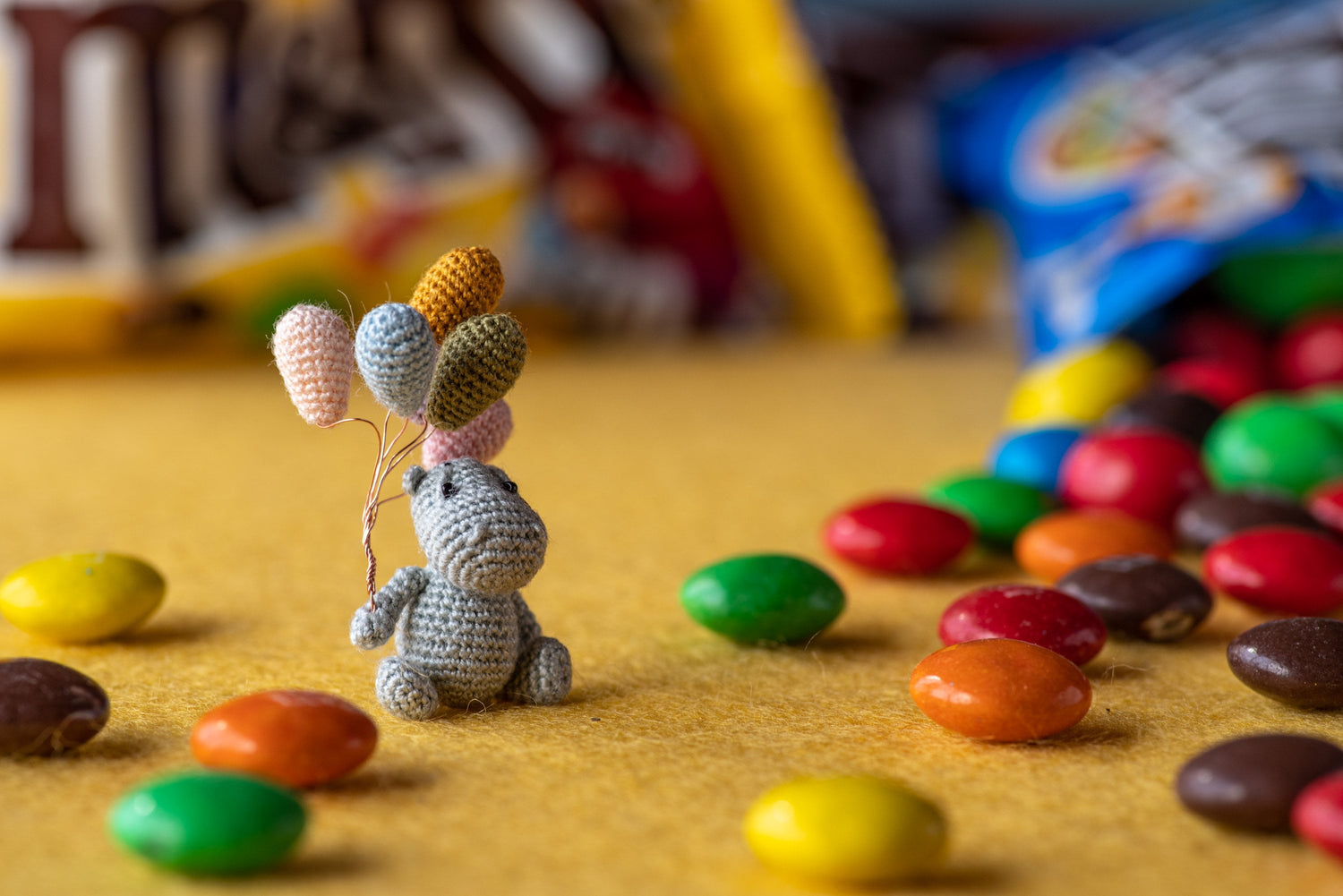 Handmade miniature crochet hippo with colorful balloons surrounded by colorful candy, whimsical collectible animal