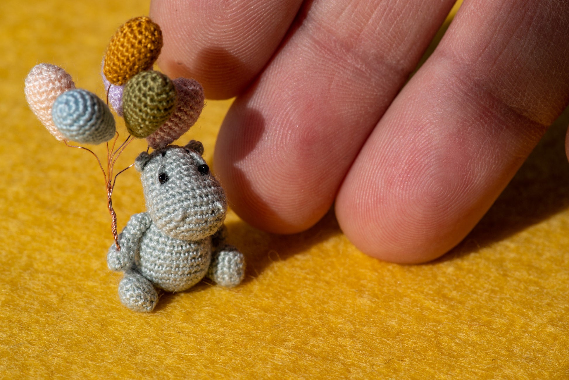 Miniature amigurumi hippo holding colorful balloons