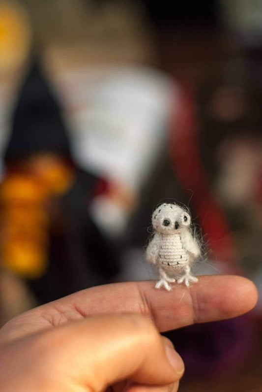 Tiny crocheted snowy owl perched on a fingertip