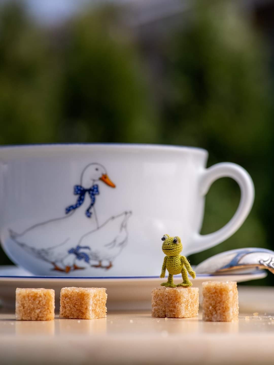 Small handmade frog figurine near spoon and duck mug