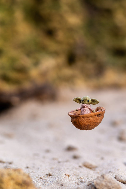 Tiny green alien crochet toy standing on sandy surface