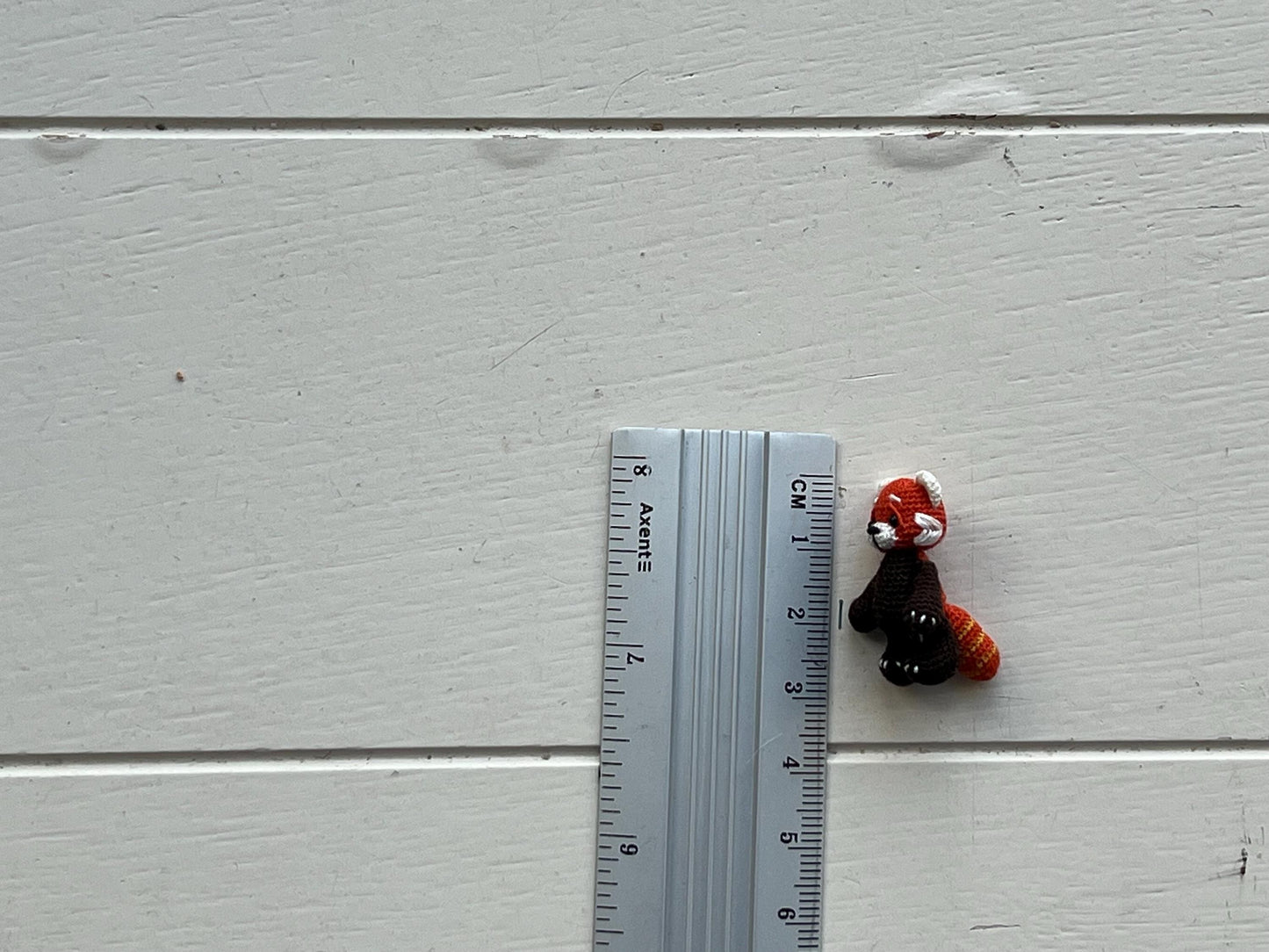 Small plush toy next to a ruler on a light gray wooden surface