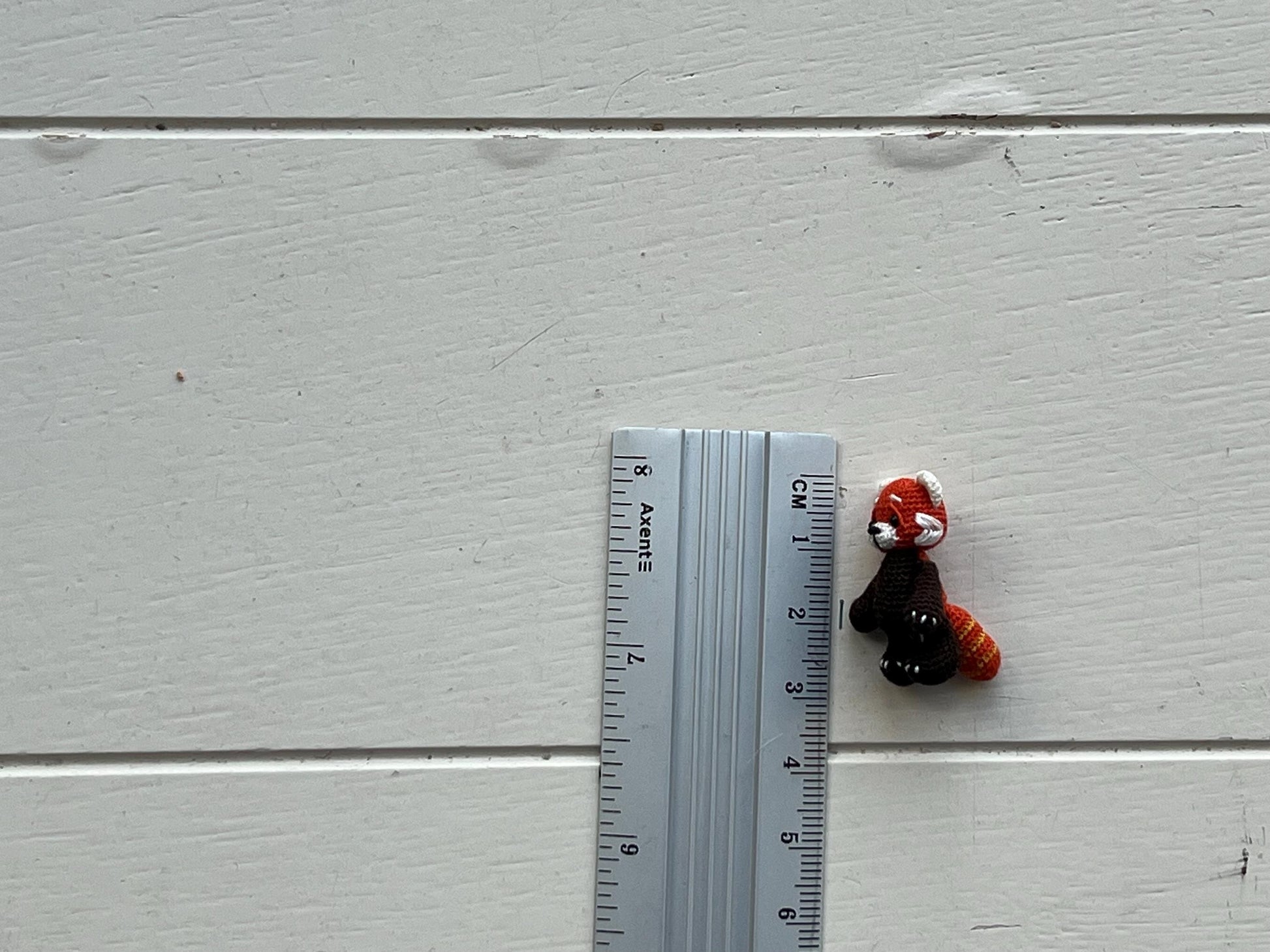Small plush toy next to a ruler on a light gray wooden surface