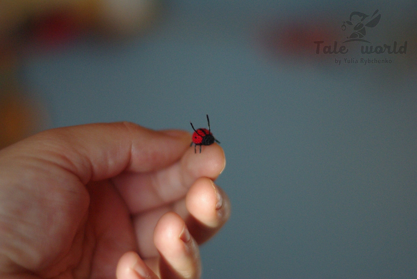 Small red and black insect on a person's finger with a blurred background