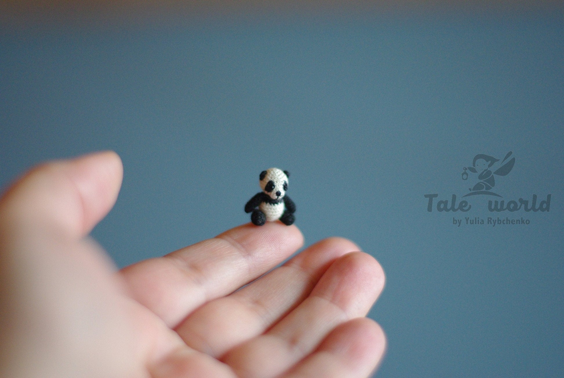 Miniature crochet panda sitting on a fingertip against soft blue background