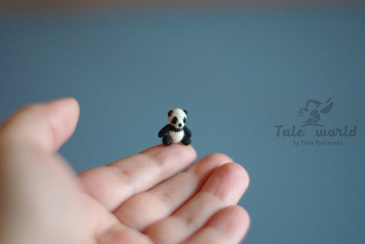 Miniature crochet panda sitting on a fingertip against soft blue background