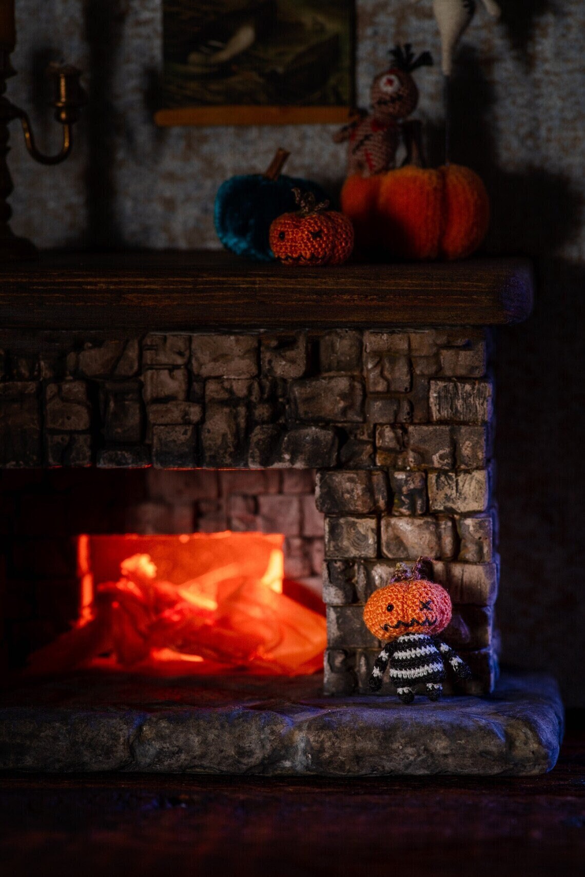 Crochet pumpkin monster glowing beside a cozy miniature fireplace.