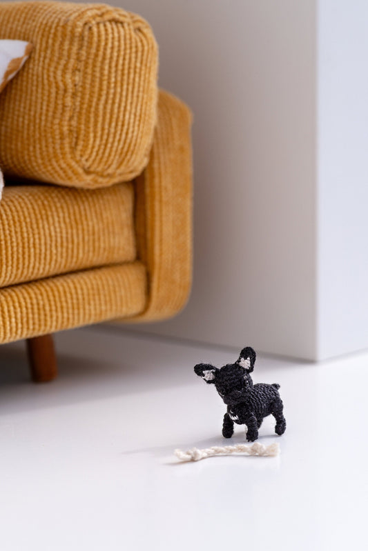 Tiny crochet French bulldog with white bone toy beside mustard couch