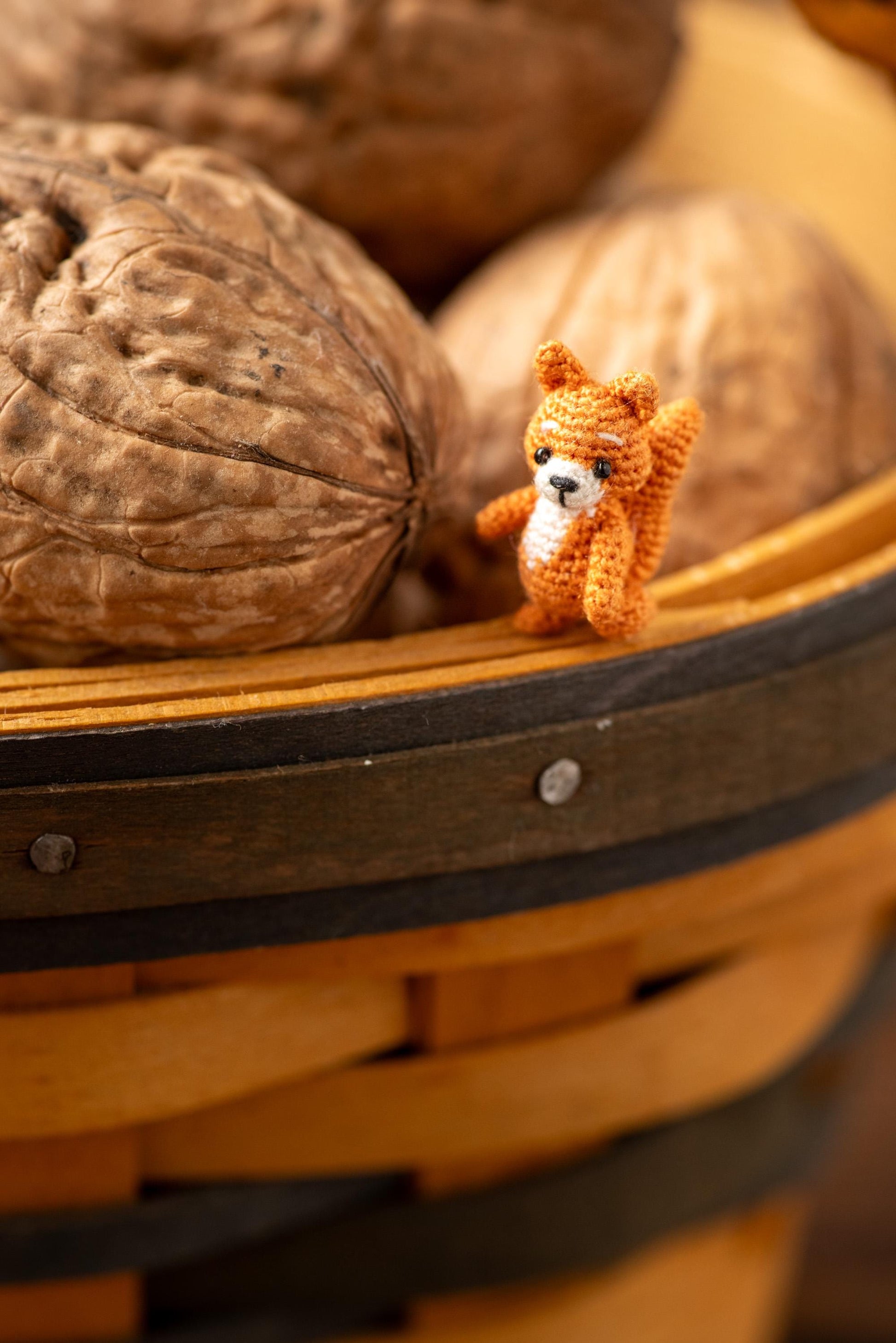 Small knitted squirrel toy among walnuts in a wooden basket