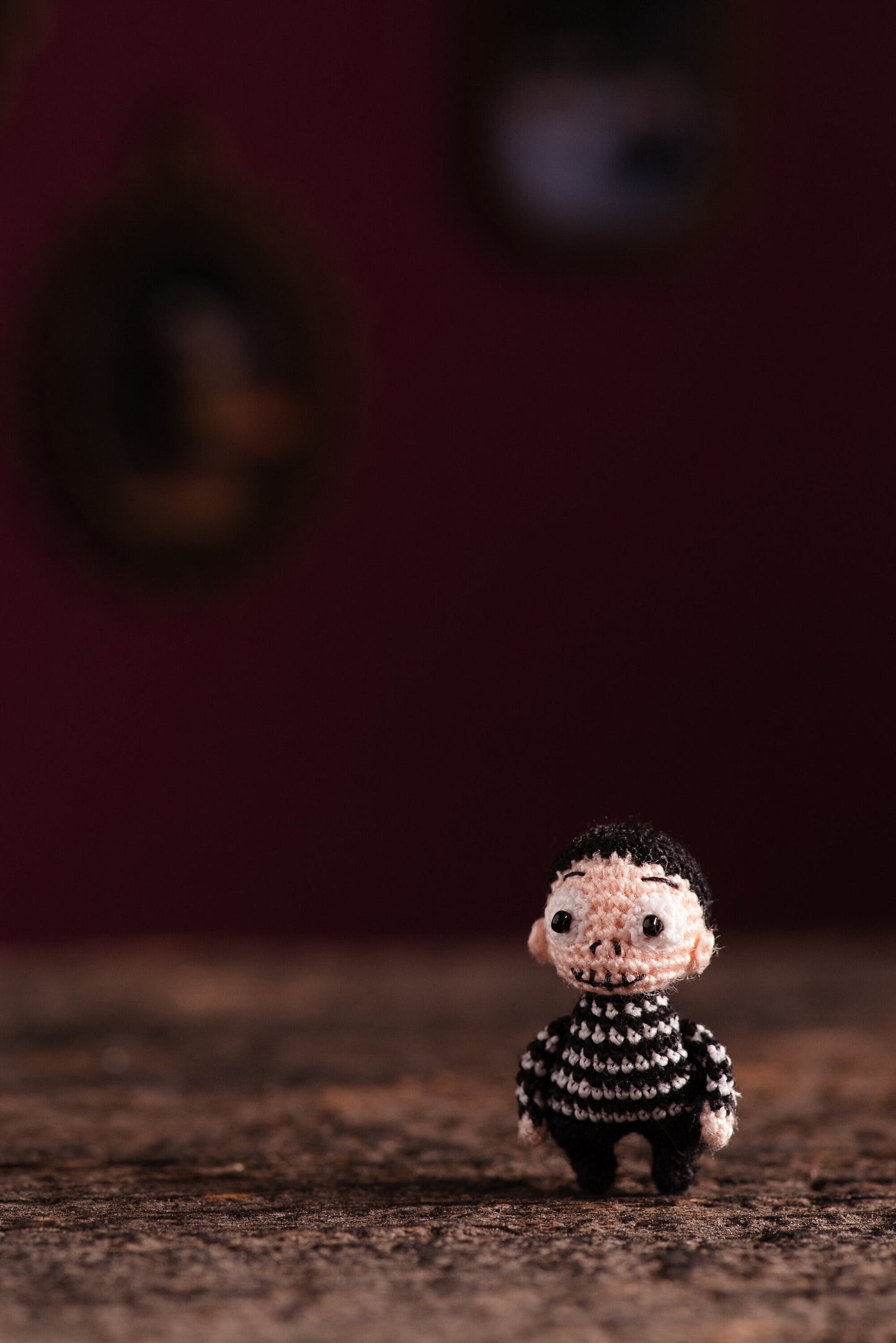 Miniature gothic boy with black striped sweater and glowing eyes standing on wooden surface.