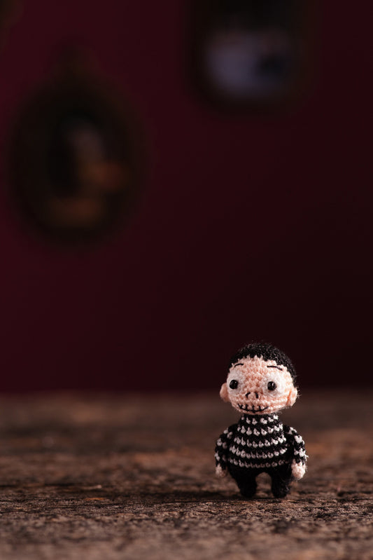 Miniature gothic boy with black striped sweater and glowing eyes standing on wooden surface.