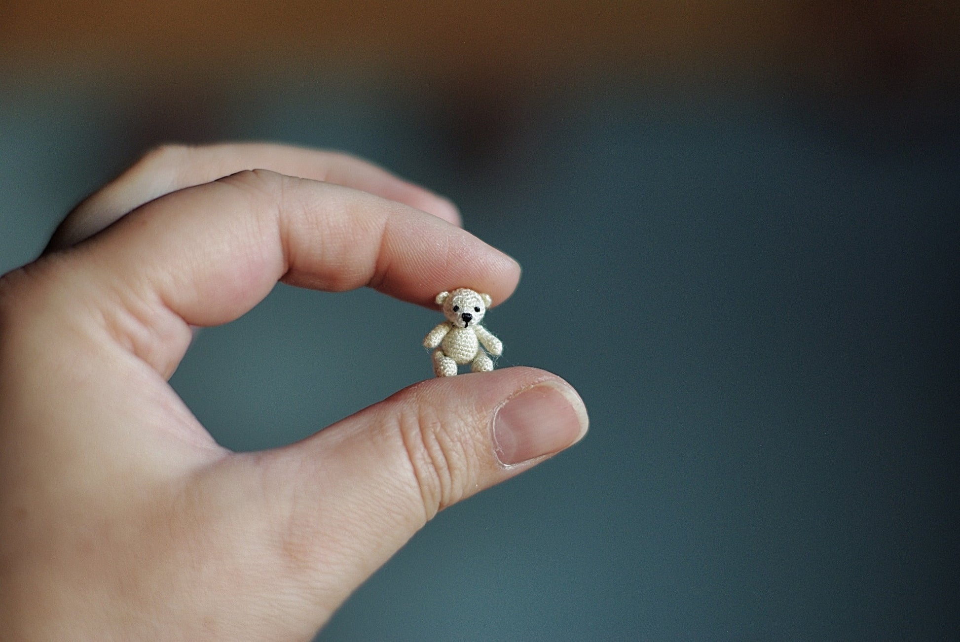 Miniature crochet teddy bear held gently between two fingers