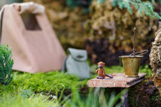 Miniature figurine of a dog standing on a stone ledge with a bucket in a garden setting.