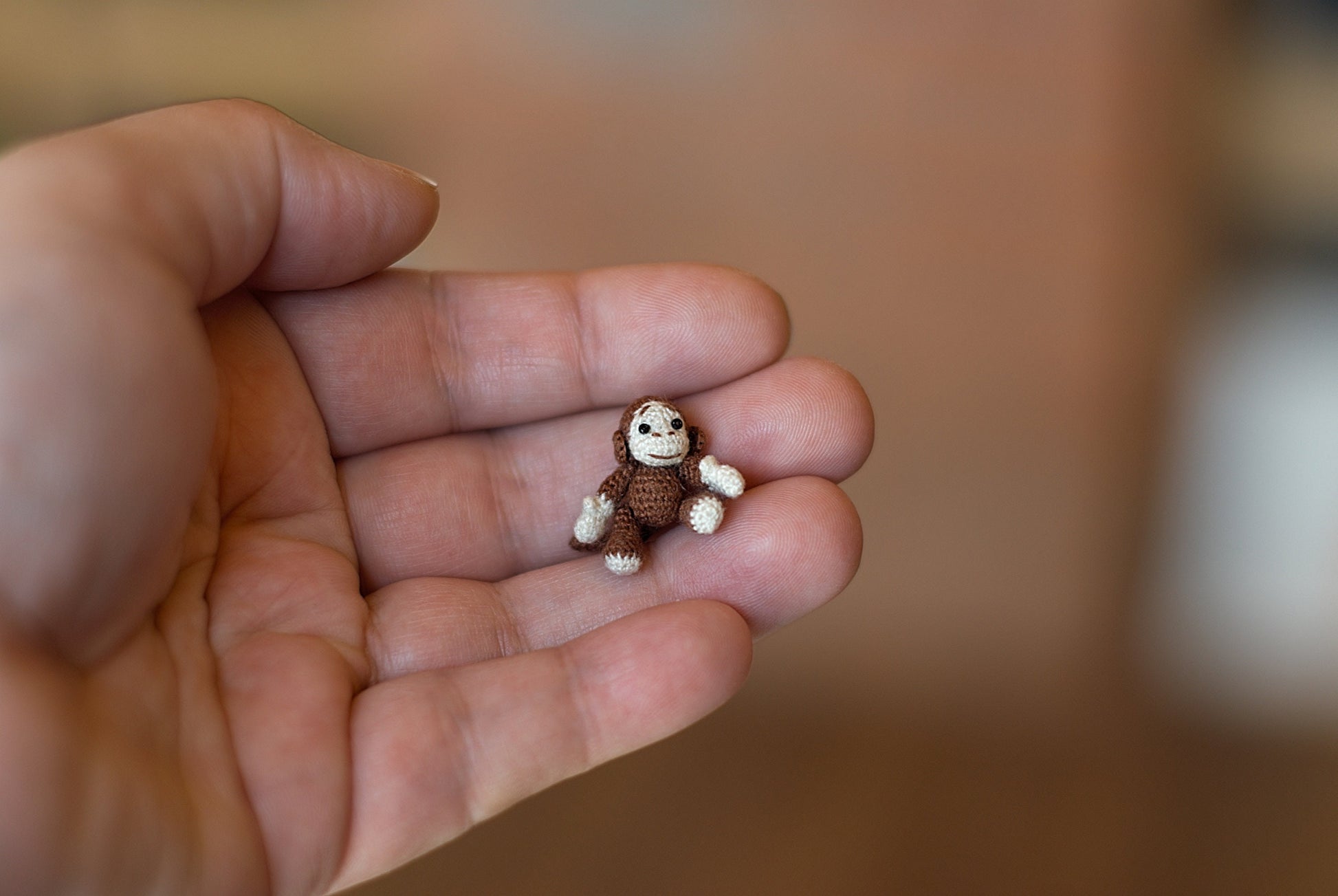 Tiny handmade crochet monkey held in a palm, brown and beige yarn