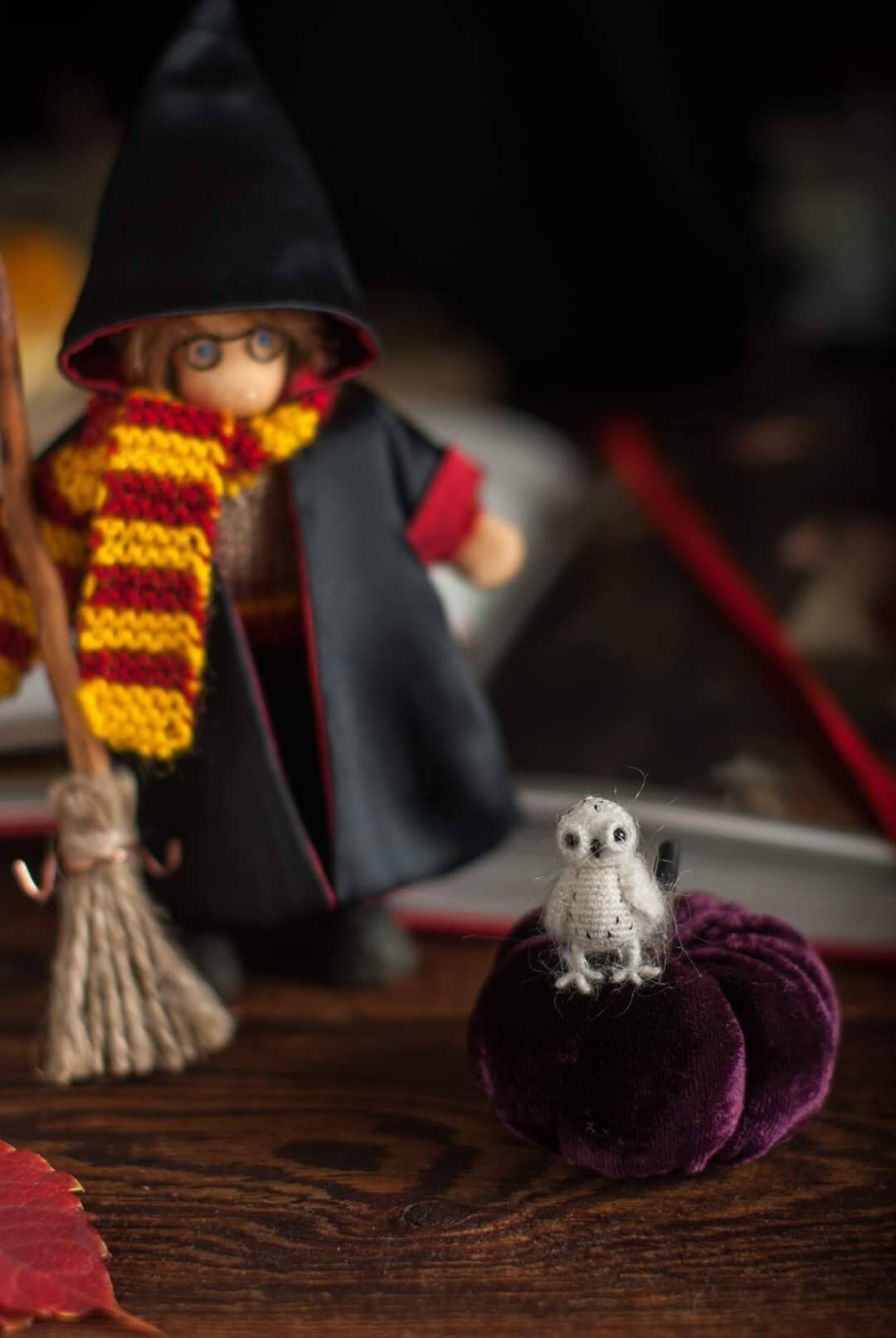 Toy figure of a wizard with a broom, scarf, and owl on a purple pumpkin with a dark background.