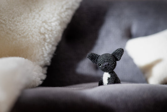 Tiny black crochet French bulldog sitting on a gray blanket