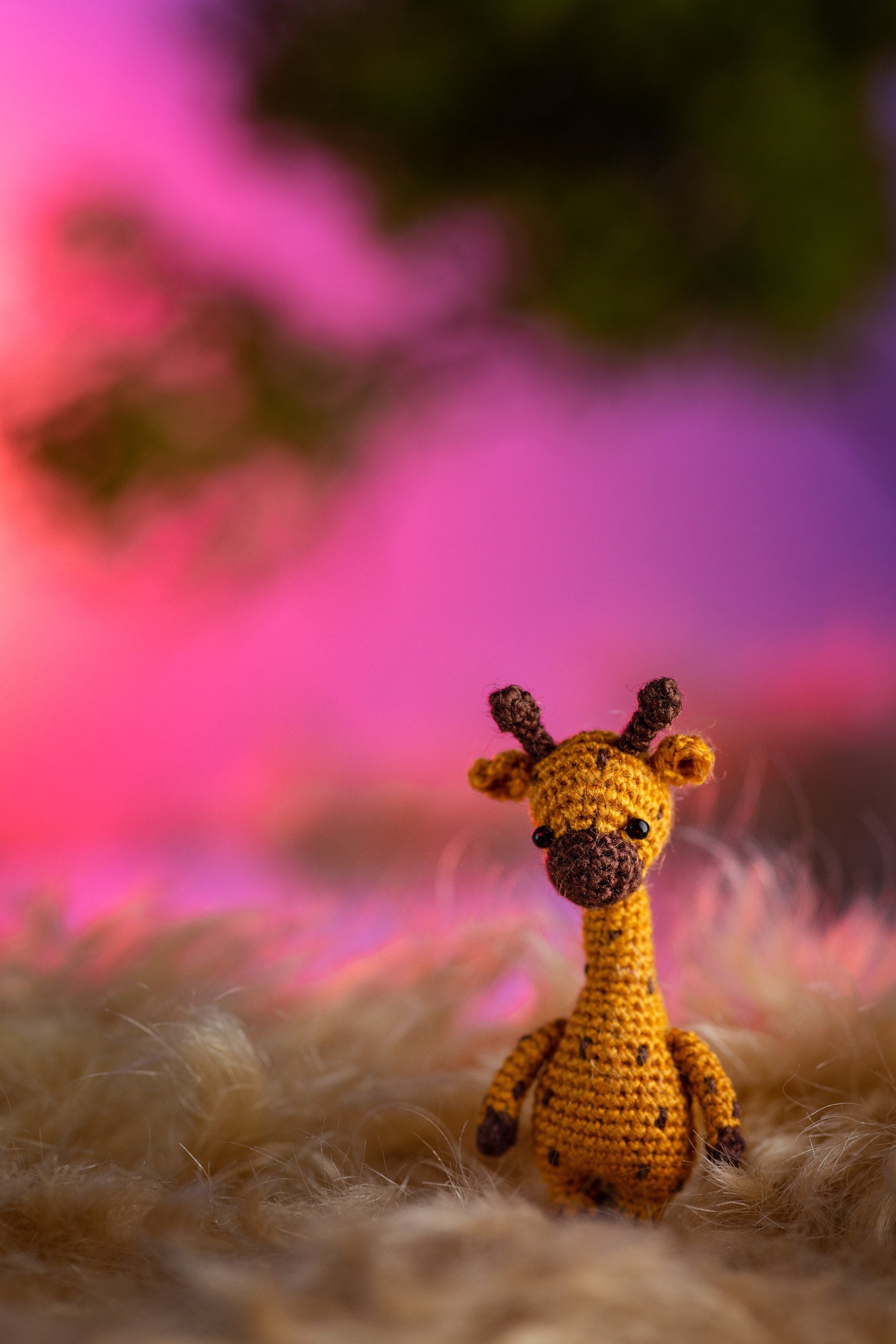 Tiny crochet giraffe standing on faux fur with dreamy pink sunset
