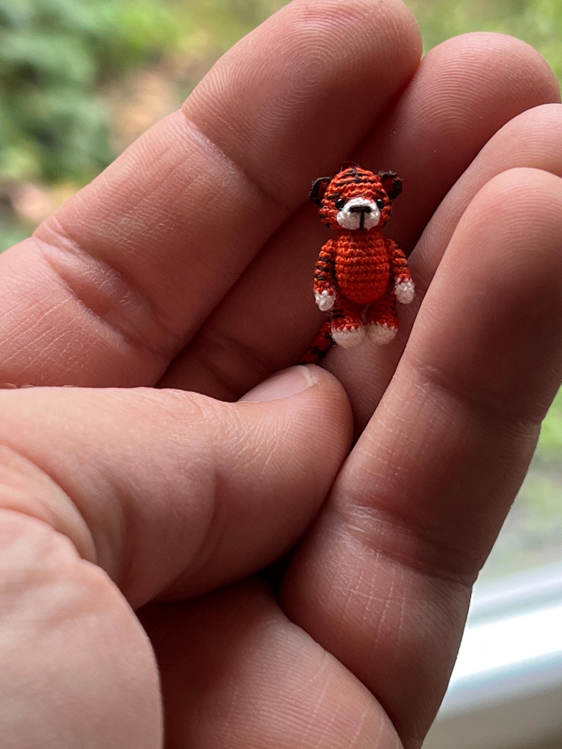 Miniature amigurumi tiger standing on fingertip in nature-inspired scene