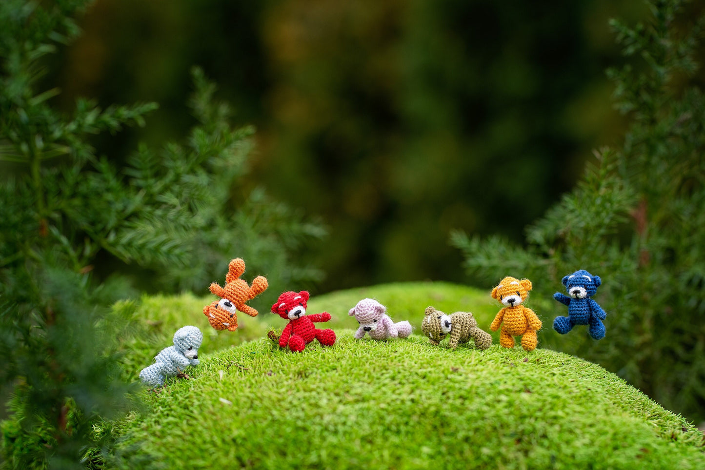 Set of colorful tiny crochet teddy bears on a mossy hill