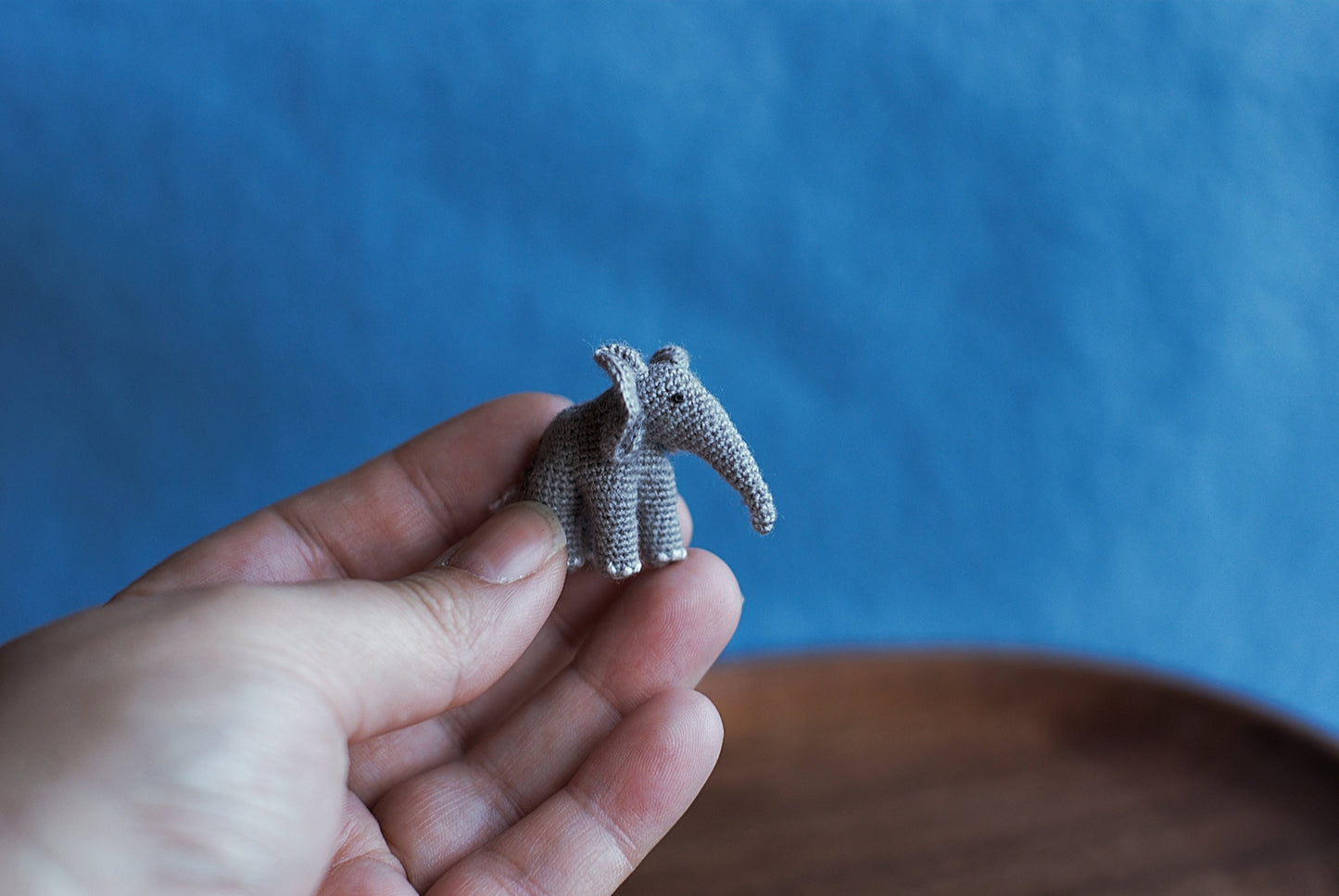 Tiny hand-crocheted grey elephant held gently in a palm