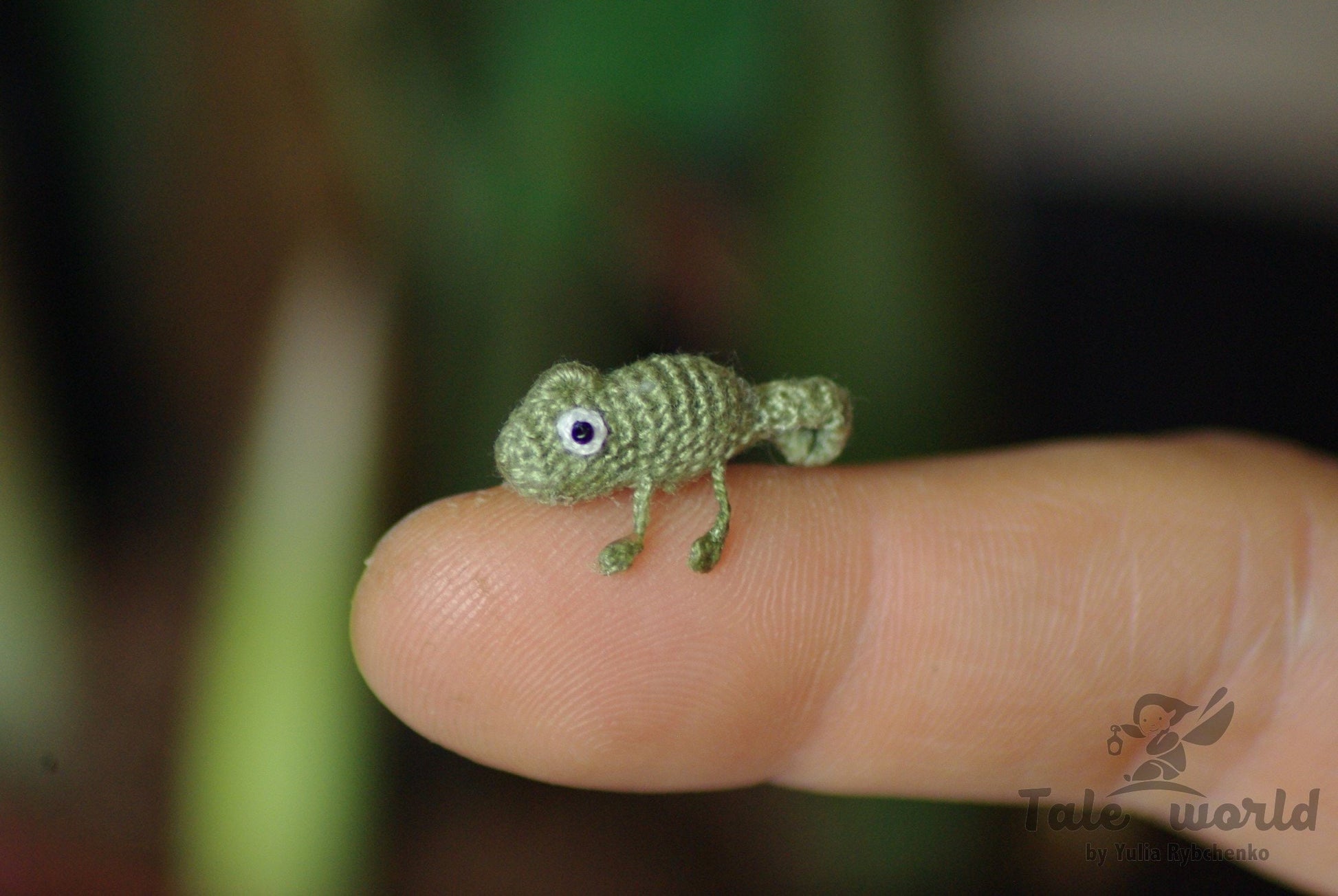 Miniature crochet chameleon resting on fingertip