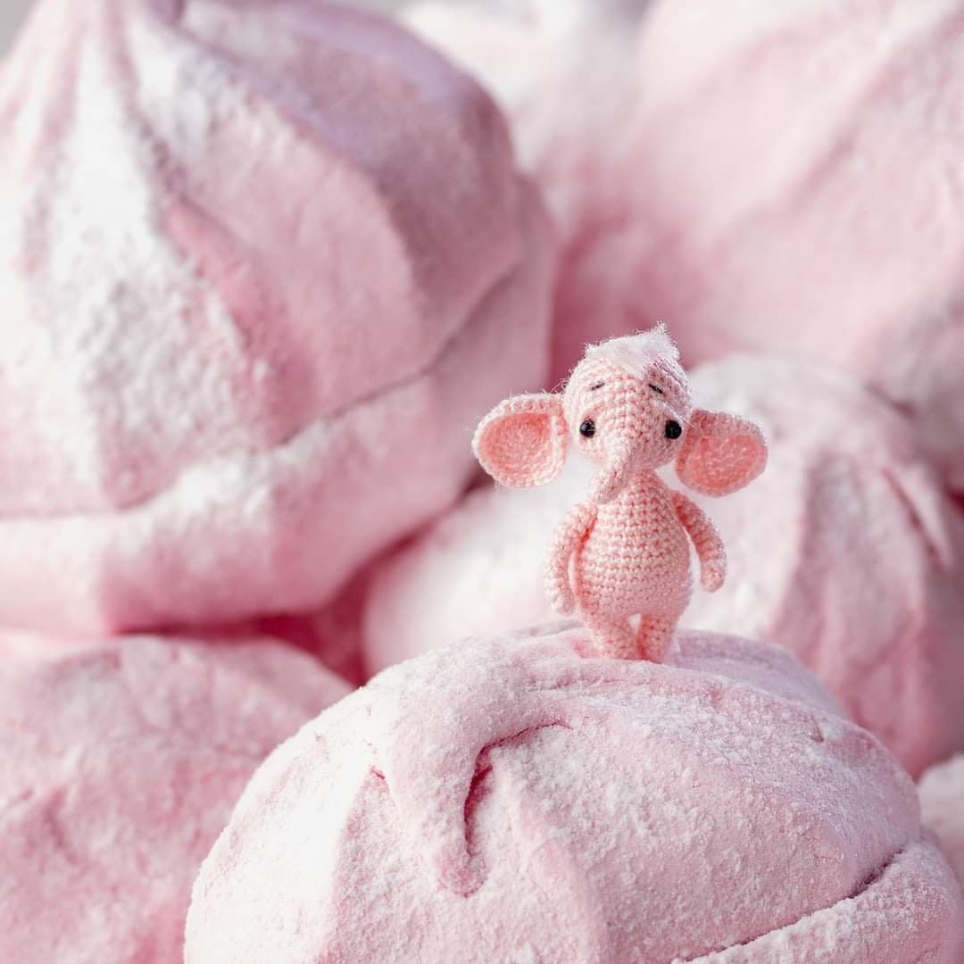 Tiny pink crochet elephant standing on pink marshmallows