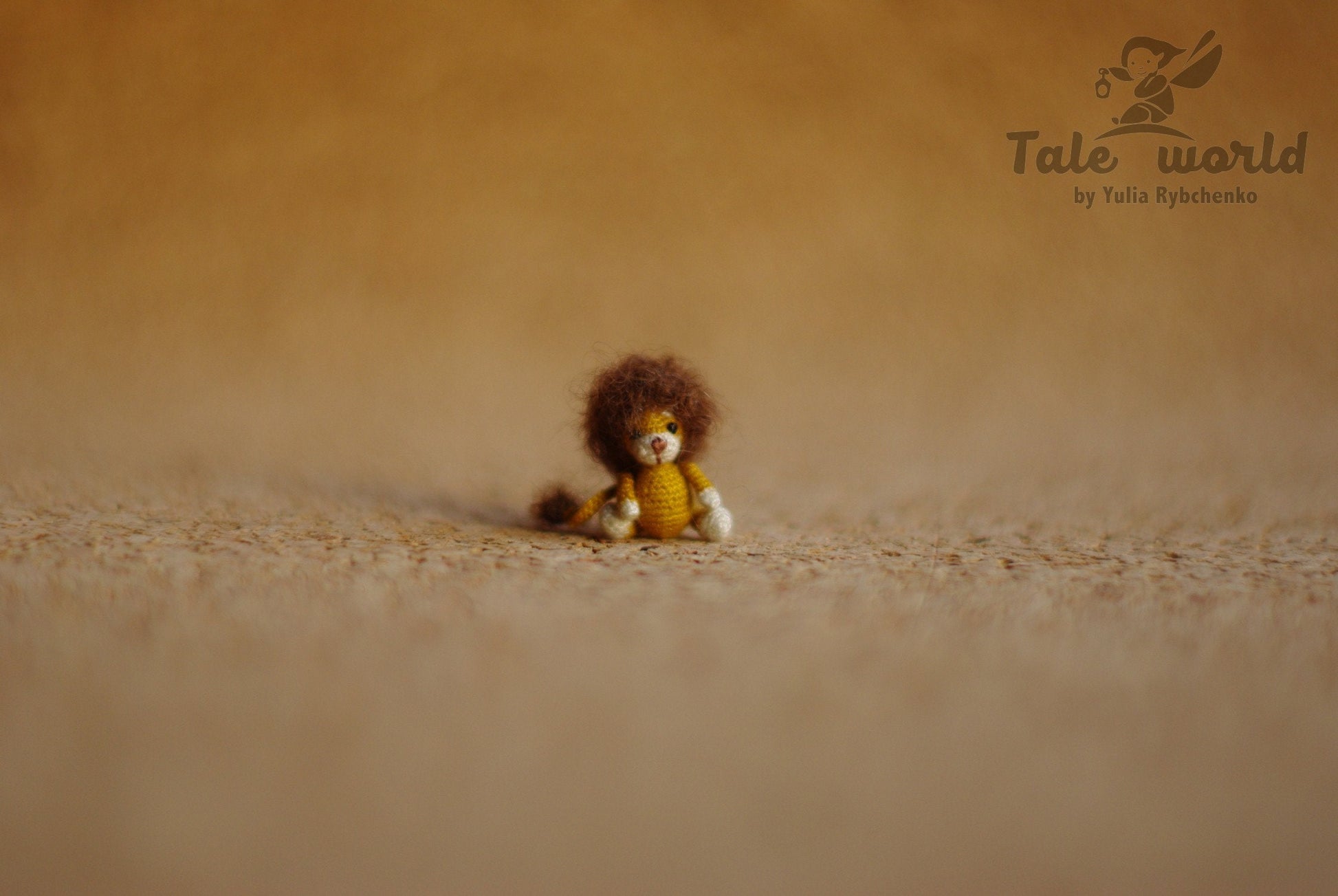 Tiny crochet lion with fluffy brown mane sitting on warm-toned fabric.