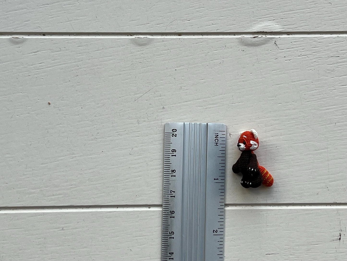 Small plush toy next to a ruler on a light gray wooden surface