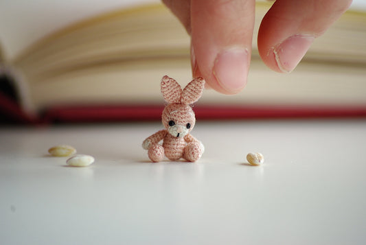 Tiny pink crochet bunny sitting on white table
