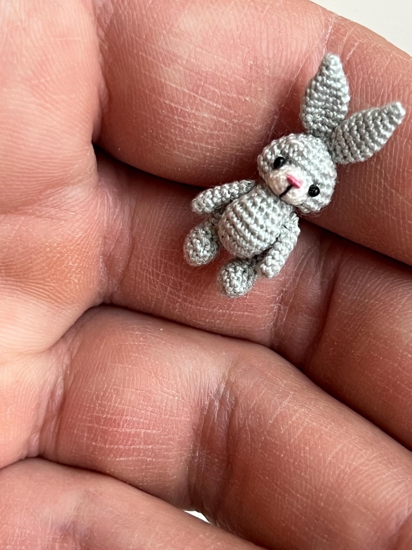 Miniature amigurumi bunny with long ears and pink nose on white background