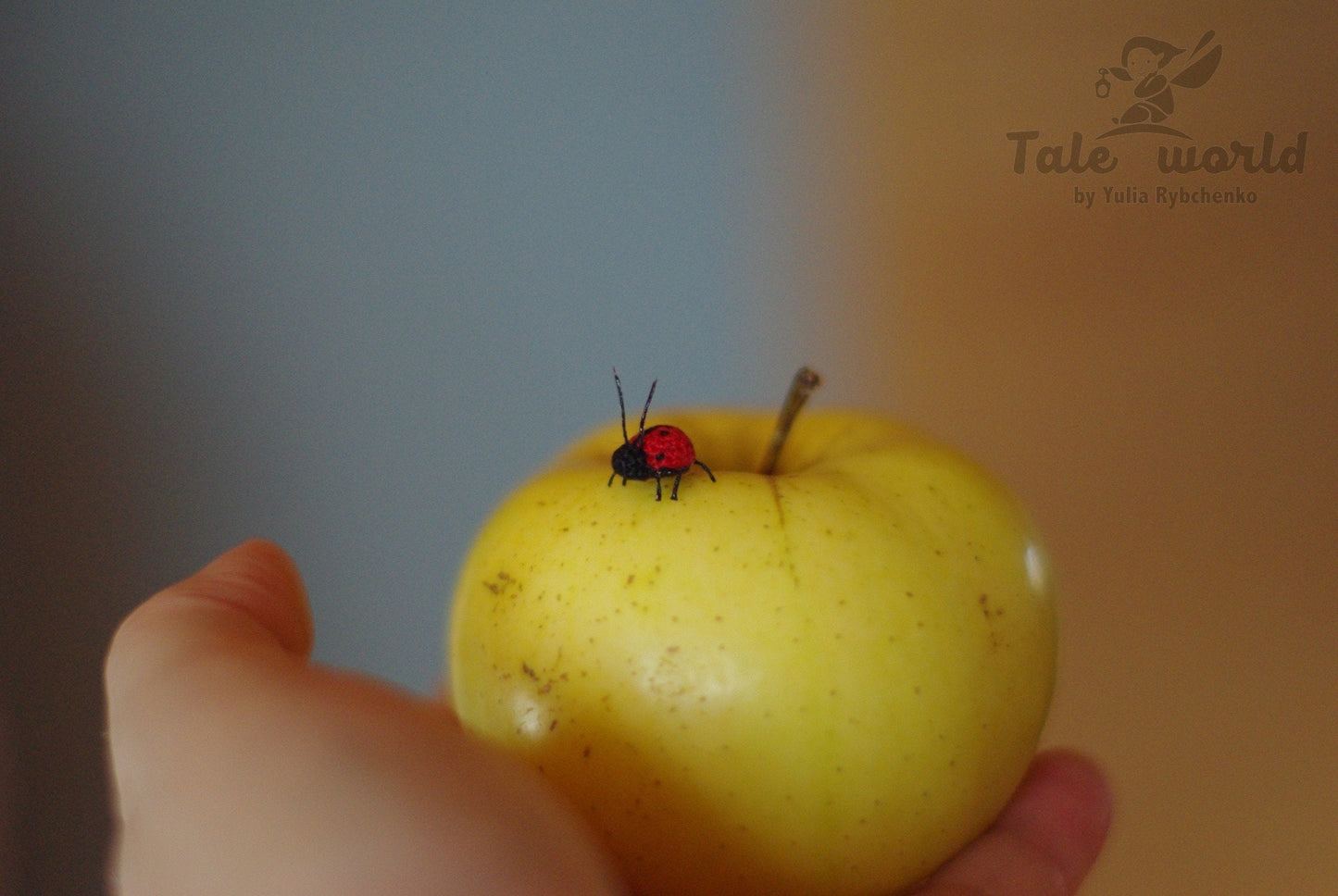 Yellow apple with a ladybug held by a hand against a blurred background