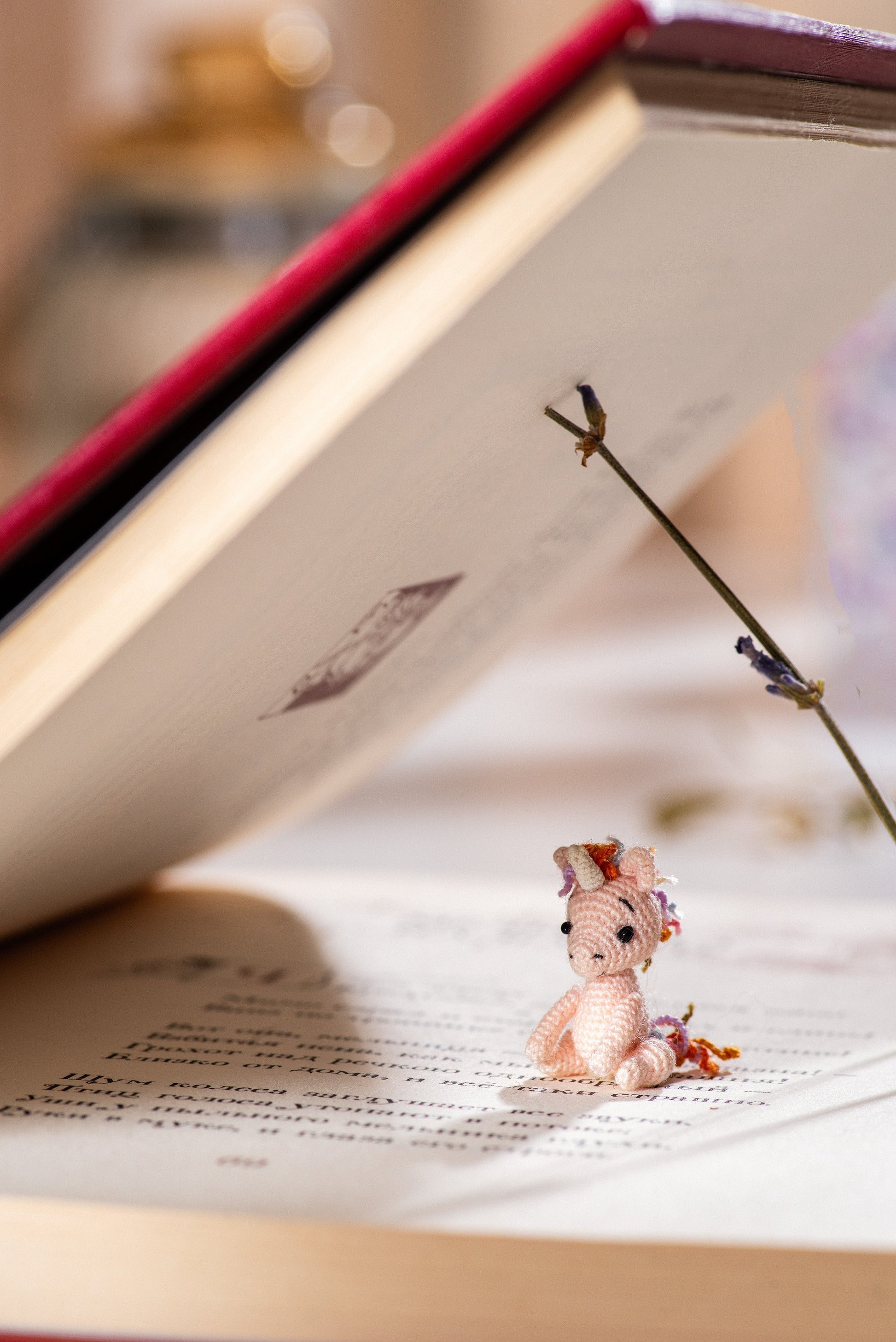 Miniature pink unicorn with rainbow mane sitting between the pages of a book