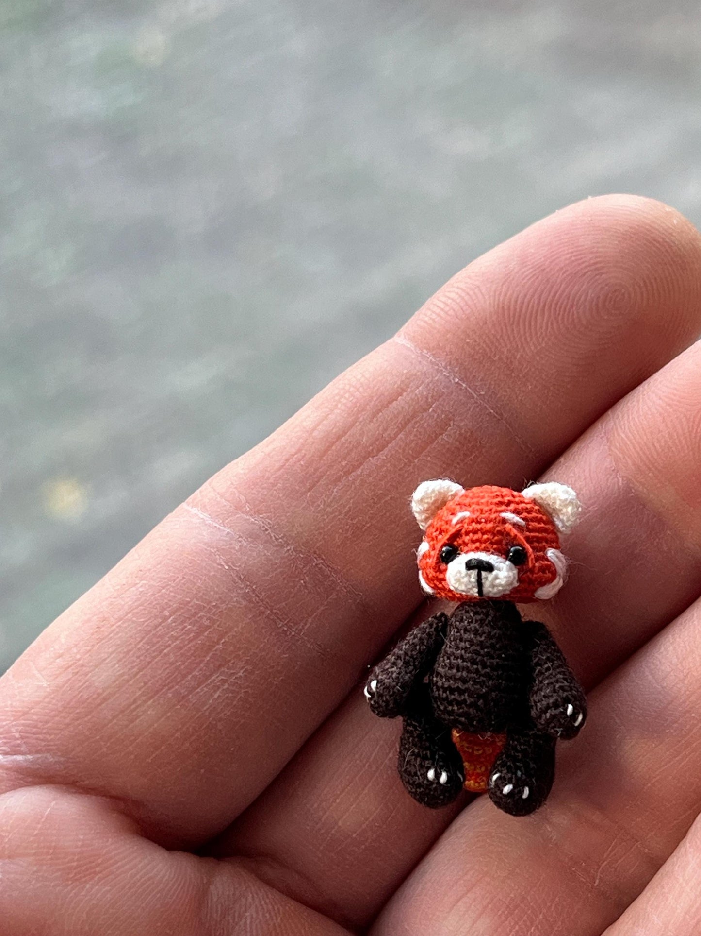 Tiny handmade crochet red panda sitting in palm