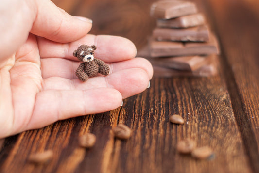 Tiny chocolate-colored crochet bear held in a palm
