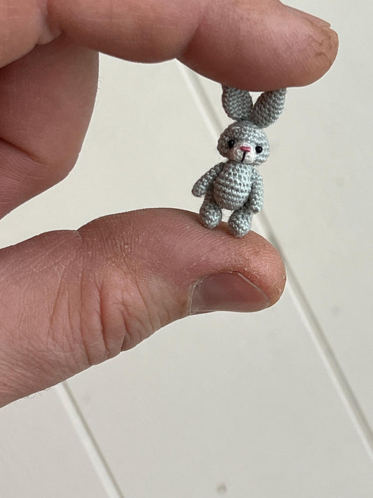 Tiny handmade grey crochet bunny held between fingers, TaleWorld miniature rabbit