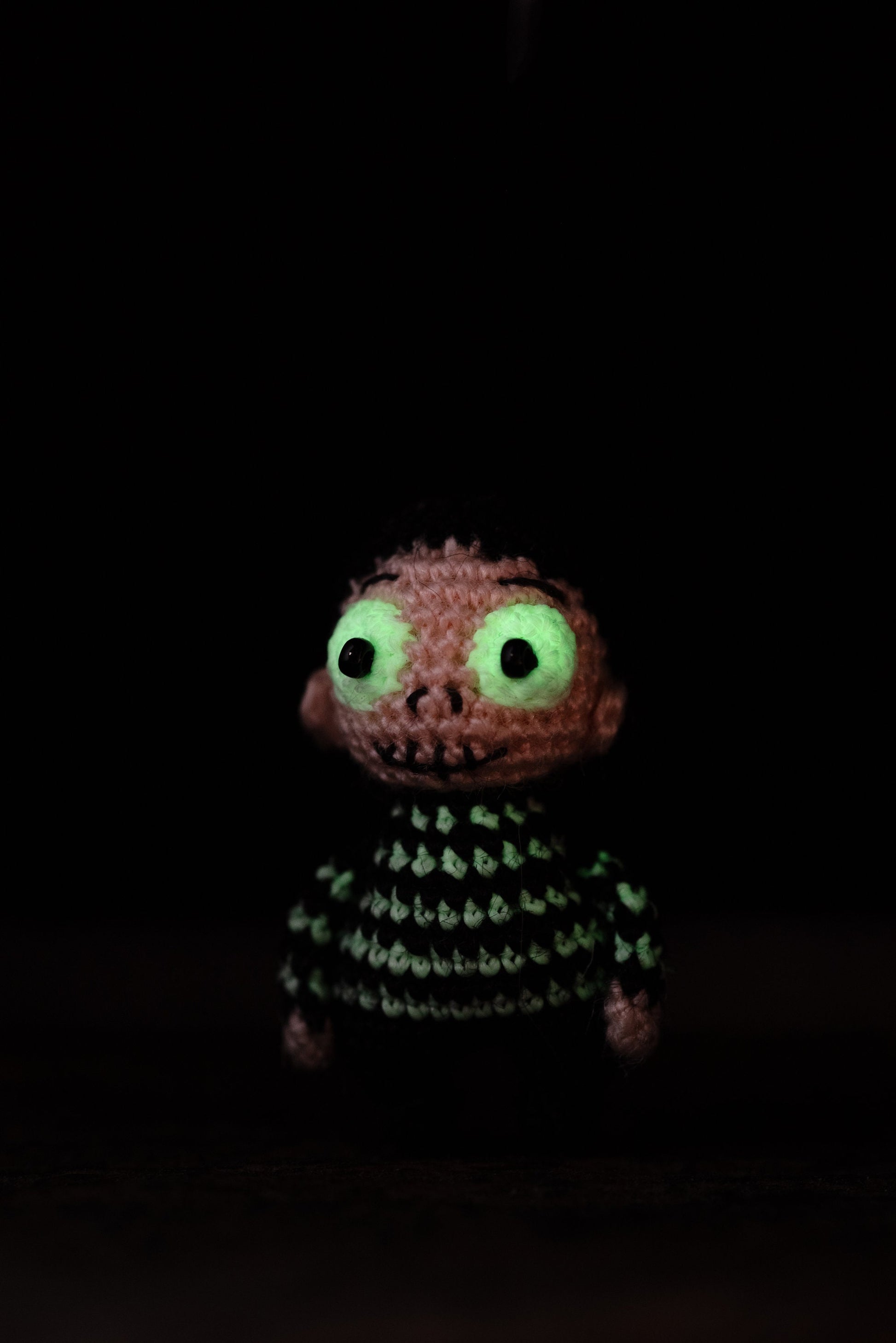 Handmade amigurumi doll with stitched mouth and luminous eyes.