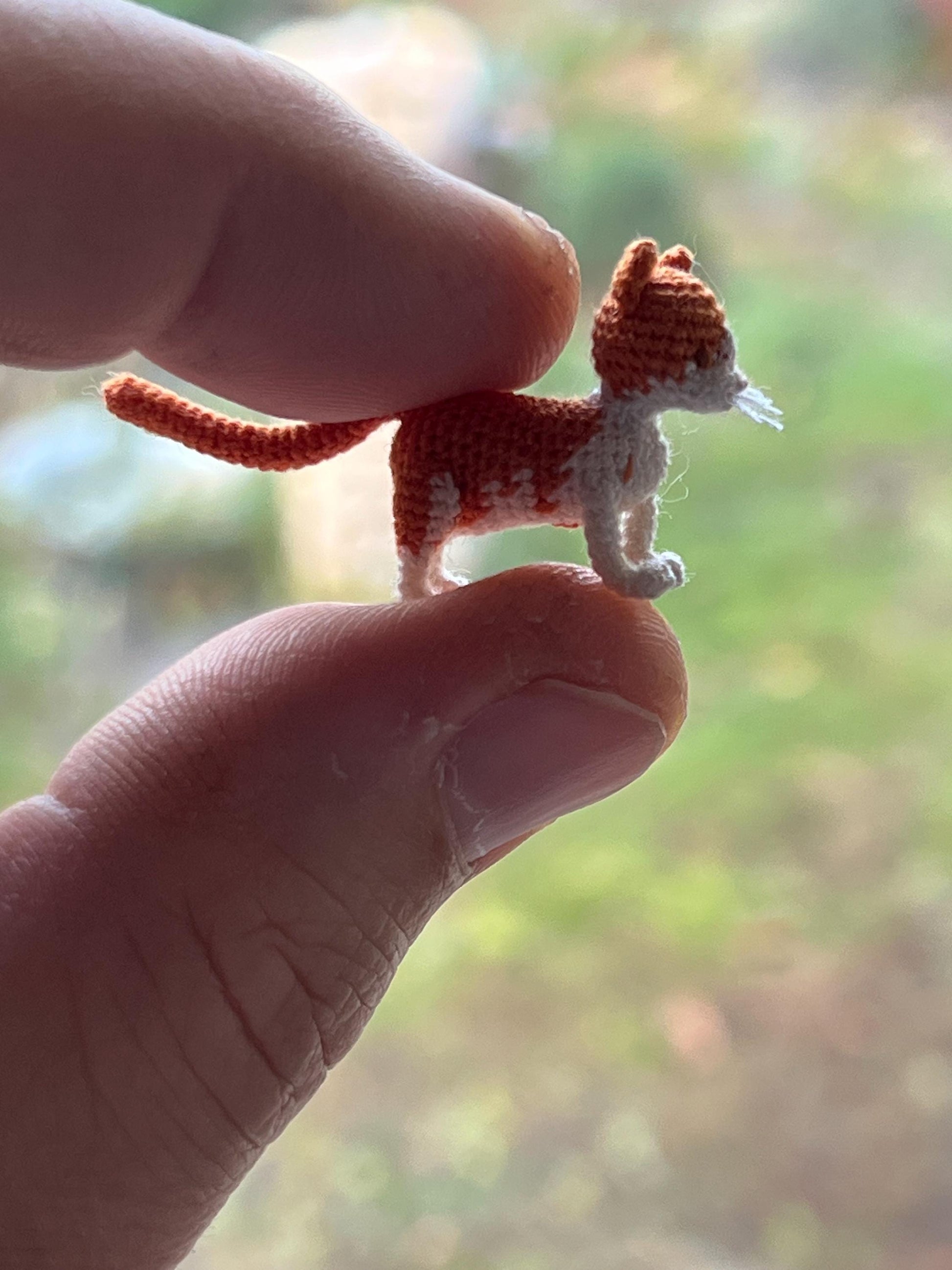 Tiny crochet cat with white whiskers held between fingers