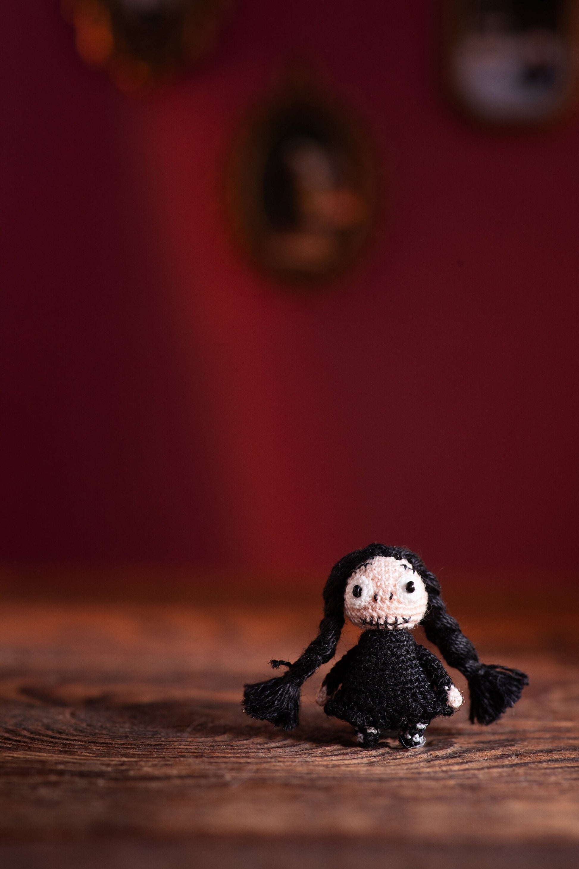 Tiny crochet doll with long black braids and stitched smirk in gothic setting.