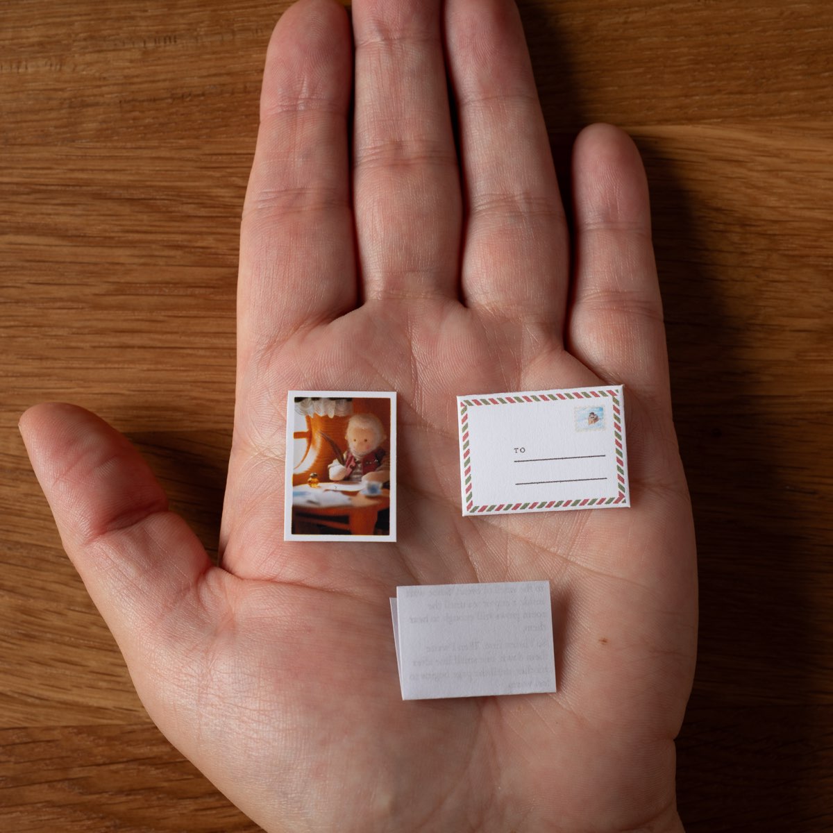 An open palm holding the three pieces of the set — the miniature postcard, the airmail-bordered envelope and the folded letter.