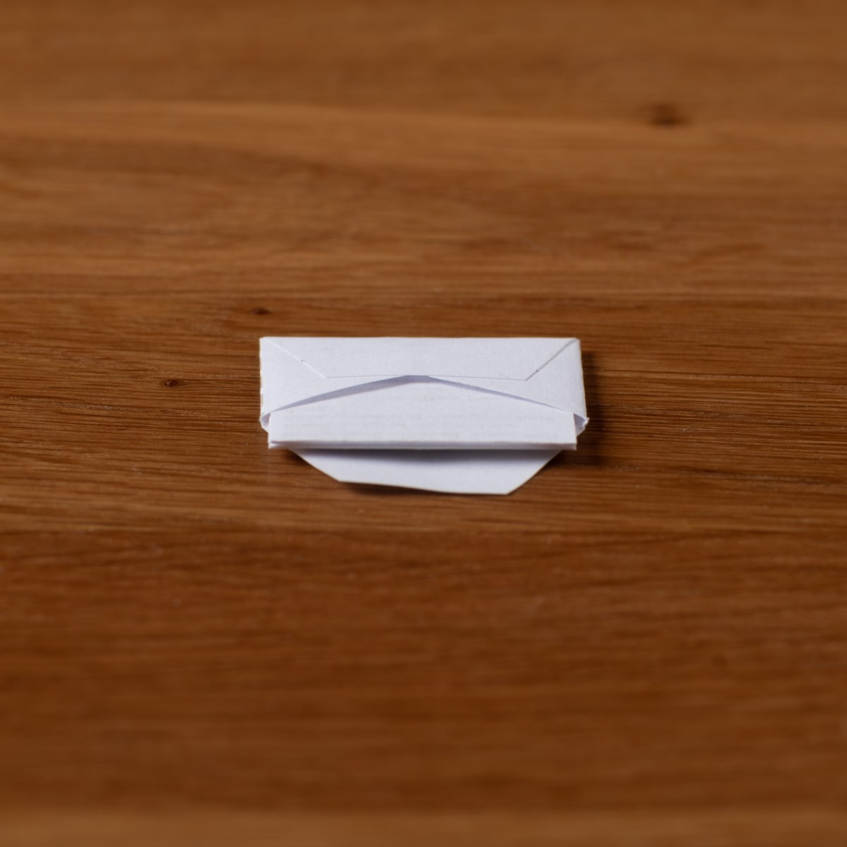 A finished miniature envelope, folded and closed, lying on a wooden table.