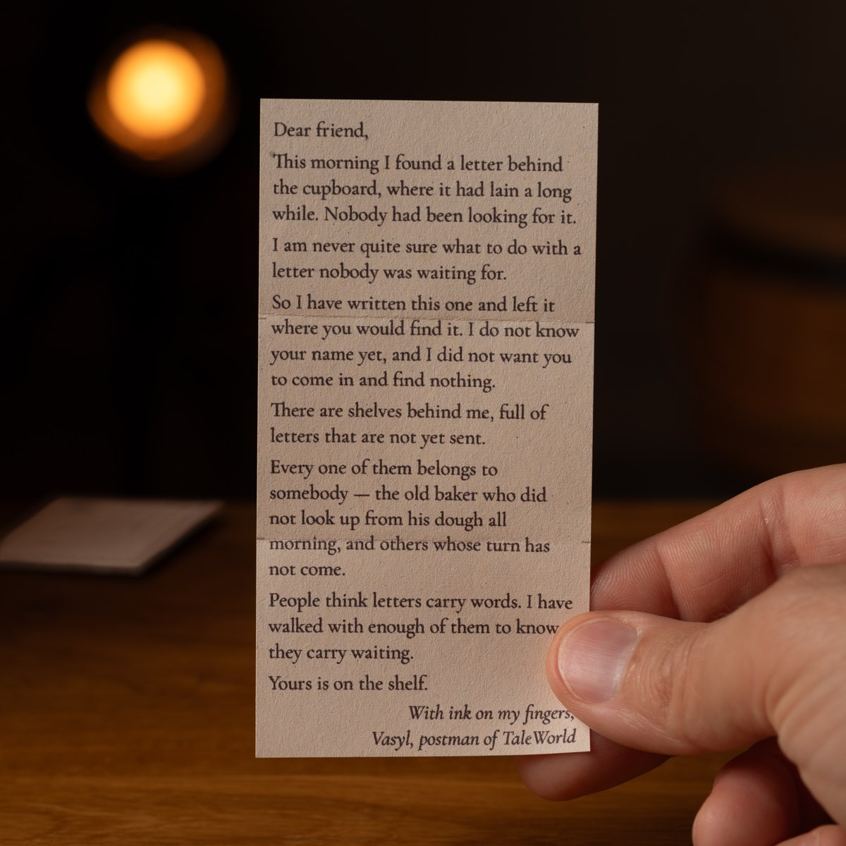 A hand holding one of Vasyl's printed letters up against a lamp in a dark room.