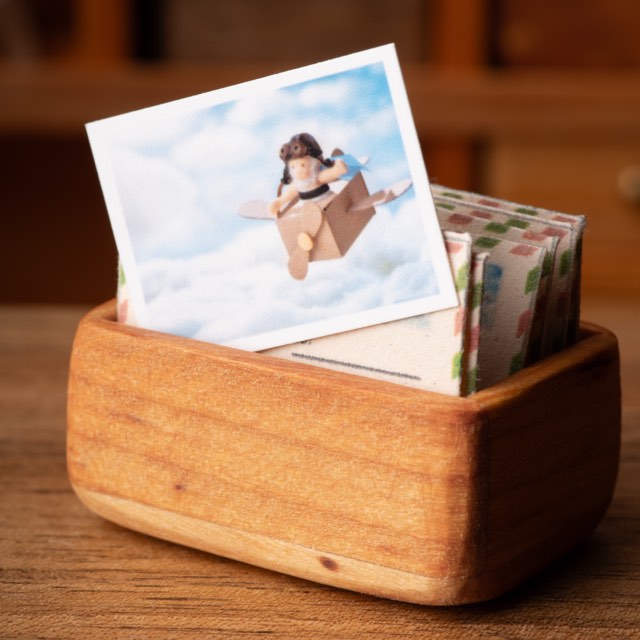 A miniature postcard standing in a wooden letter tray among airmail envelopes.