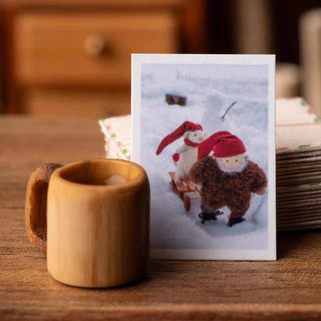 A miniature postcard standing against a stack of airmail envelopes beside a small turned wooden mug.