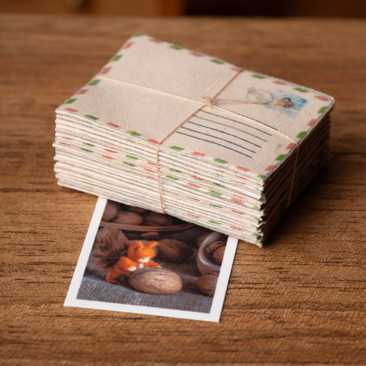 A bundle of tiny airmail envelopes tied with thread, resting on a miniature postcard on a wooden table.
